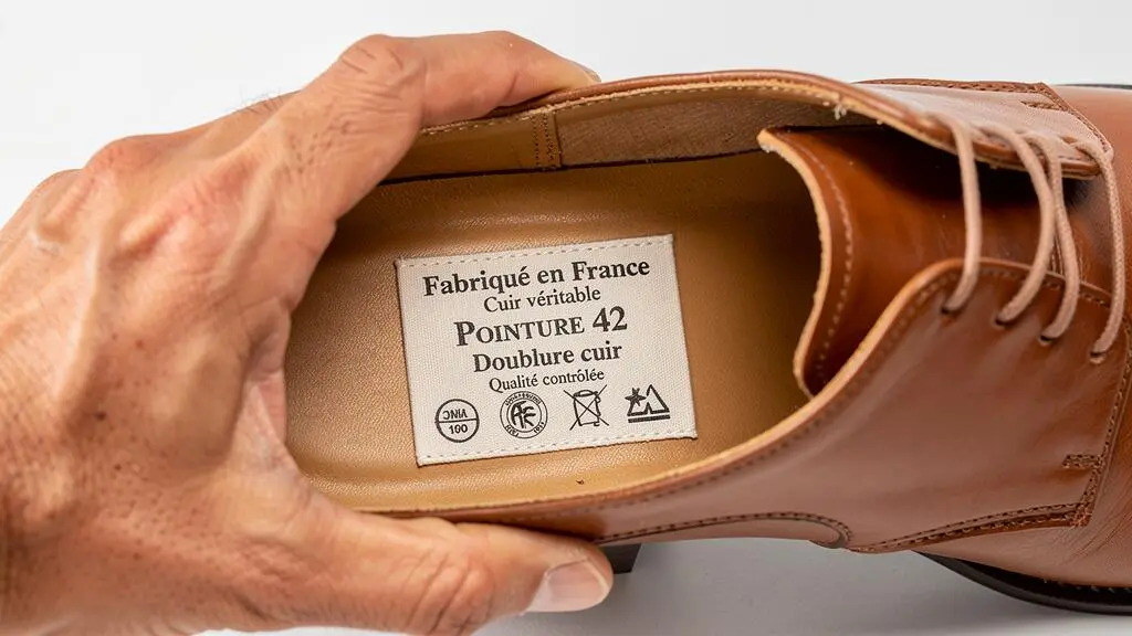 Main tenant une chaussure en cuir pour montrer l'étiquette intérieure avec les informations d'origine et de fabrication